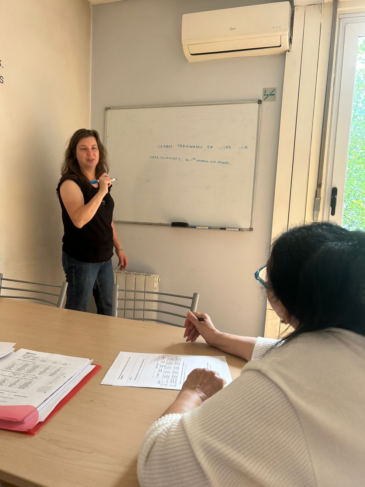 A Verbum teacher explaining Spanish grammar at the whiteboard while a student works at the table